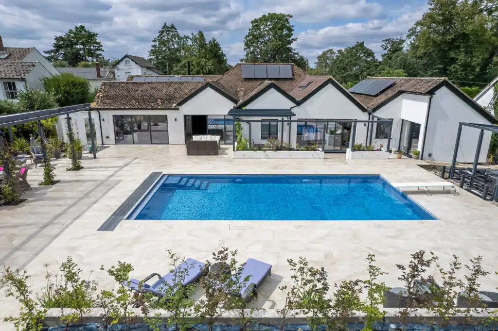 Aerial view of a swimming pool with porcelain paving and copings around a house