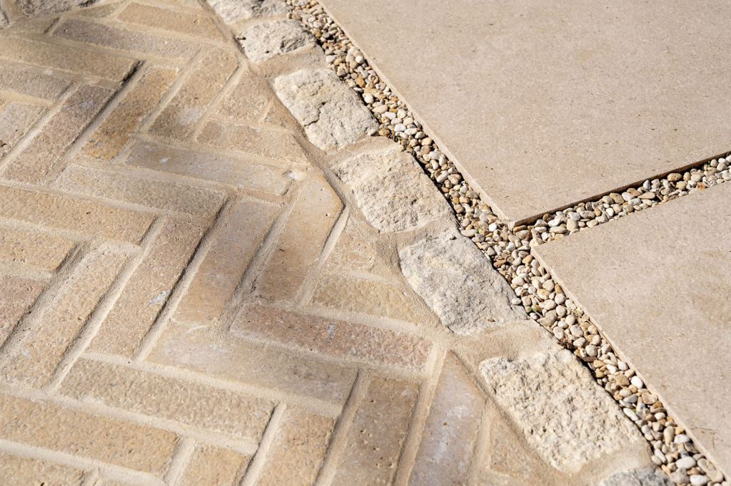 Close view of Purbeck limestone setts in herringbone with a pitcher border, meeting La Roche limestone slabs set in gravel joints