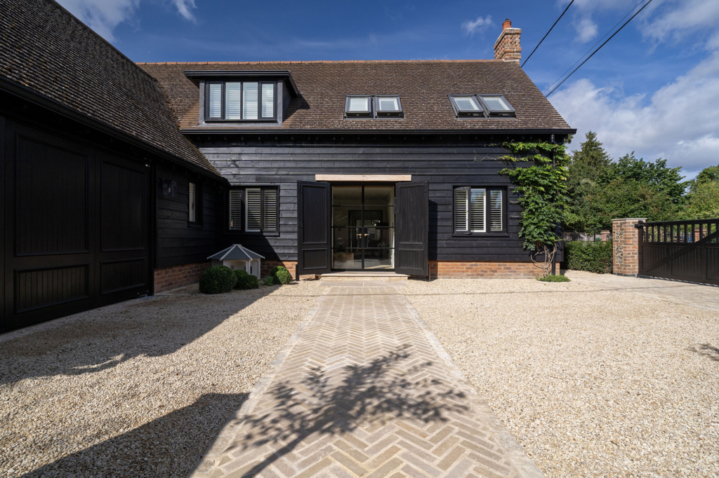 Herringbone Purbeck limestone sett path crossing a Cotswold Shale gravel forecourt to the front door of a black weatherboarded house