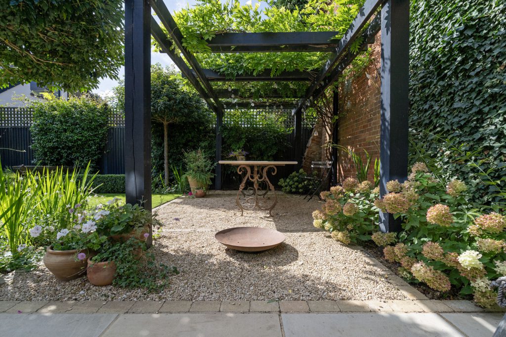 Black timber pergola over a gravel seating area with a fire bowl, edged by La Roche limestone paving and hydrangeas